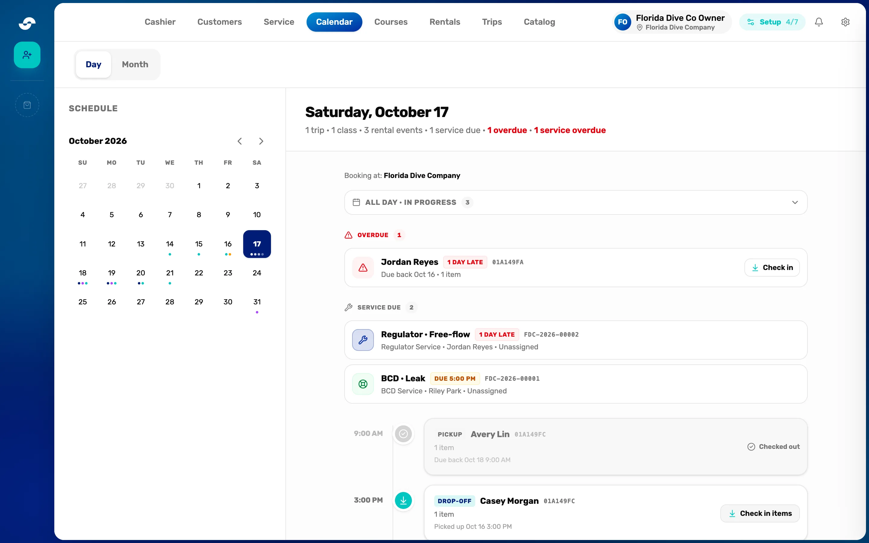 The calendar in Day view for Saturday, October 17: Day and Month at the top, the Schedule month on the left with colored dots under busy days, the summary 1 trip, 1 class, 3 rental events, 1 service due, 1 overdue, 1 service overdue, and the day's list with Booking at: Florida Dive Company